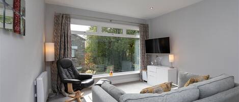 A modern living room with a grey sofa, a black chair, a TV, and a window with curtains.