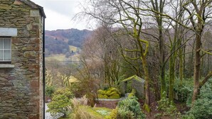 A stone building with a window, surrounded by a garden with various plants and trees. - Silver Howe (Ambleside)