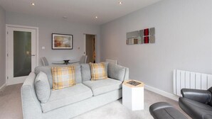 A modern living room with a grey sofa, a small white side table, and a black leather chair. - Silver Howe (Ambleside)