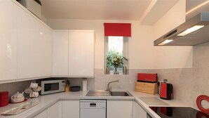 A modern kitchen with white cabinets, a microwave, a dishwasher, a sink, and a window with a red blind. - Silver Howe (Ambleside)