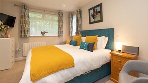 A bedroom with a bed, a bedside table with a lamp, a TV, a window with curtains, and a framed picture on the wall. - Silver Howe (Ambleside)