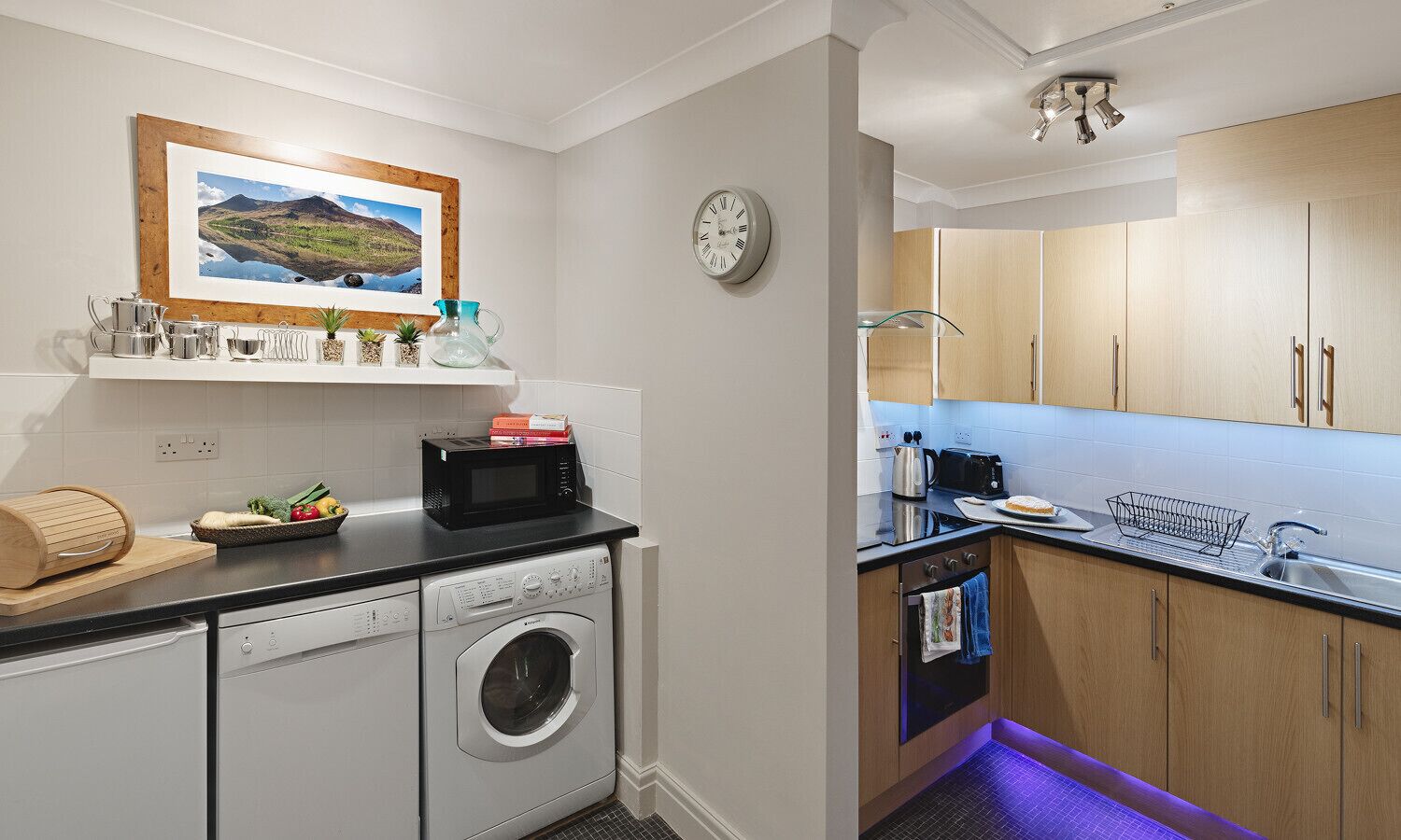 A compact kitchen with a washing machine, microwave, and wooden cabinets.