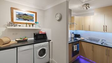 A compact kitchen with a washing machine, microwave, and wooden cabinets.
