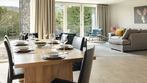 Een moderne eethoek met een houten tafel voor zes personen, een bank en een groot raam met gordijnen.