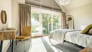 Een slaapkamer met een bed, een stoel, een bureau en een groot raam met gordijnen.