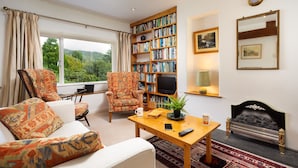 Una sala de estar con sofá, sillones, una mesa de centro, chimenea, estantería y televisor.