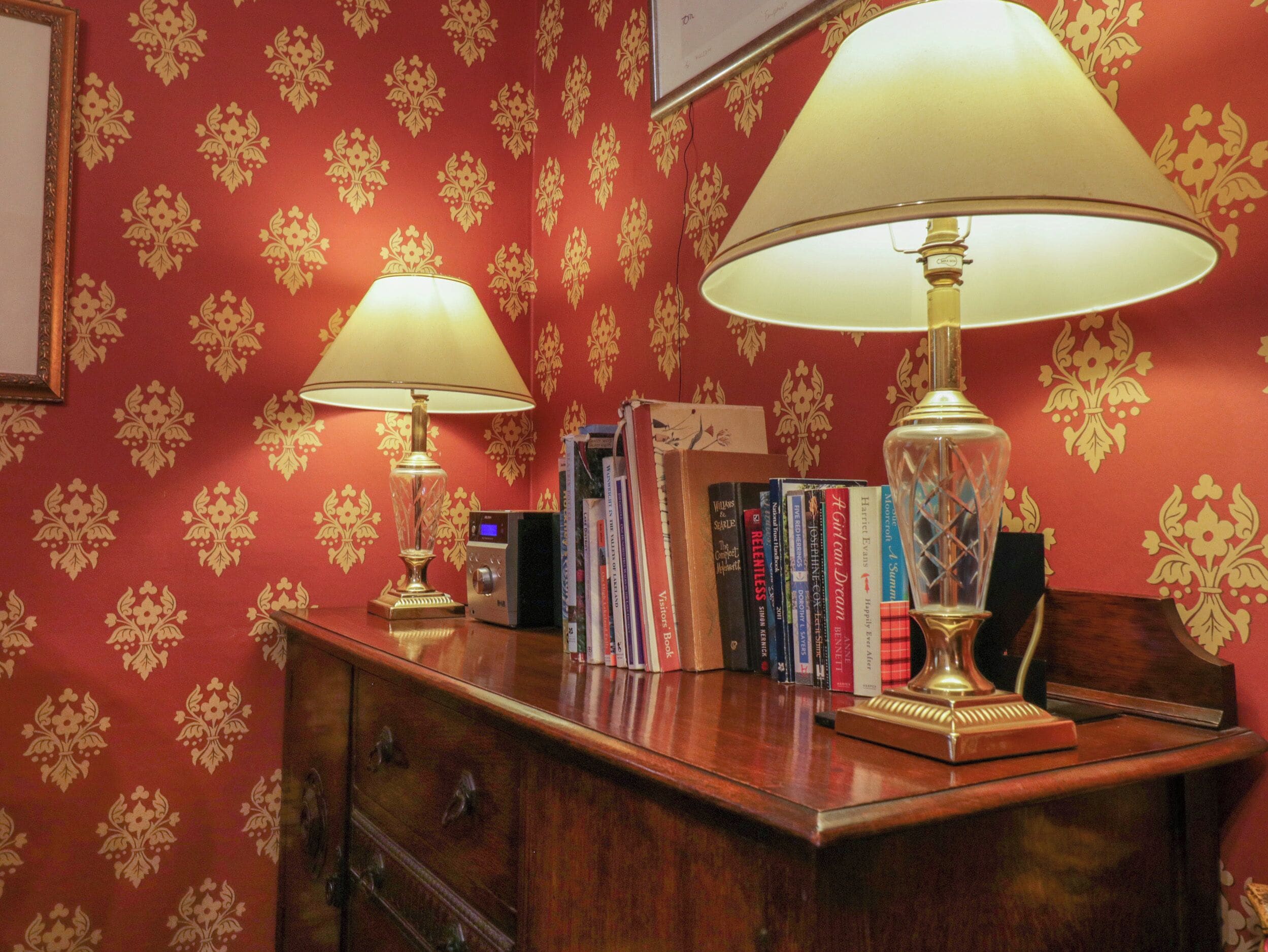 A room with a wooden desk, two lamps, and a bookshelf with books.