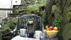 A metal chair with a newspaper, a coffee pot, and a fruit basket. - The Rockery Suite (Ambleside)