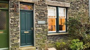 Ein Steinhaus mit grüner Tür und einem Fenster mit weißen Fensterläden.