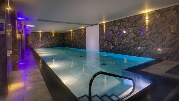 Ein moderner, überdachter Pool mit klar blauem Wasser, umgeben von Steinwänden und ausgestattet mit einer Poolleiter.