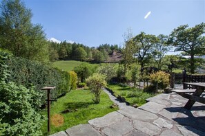 A stone pathway leading to a picnic area with a view of a green landscape and trees.