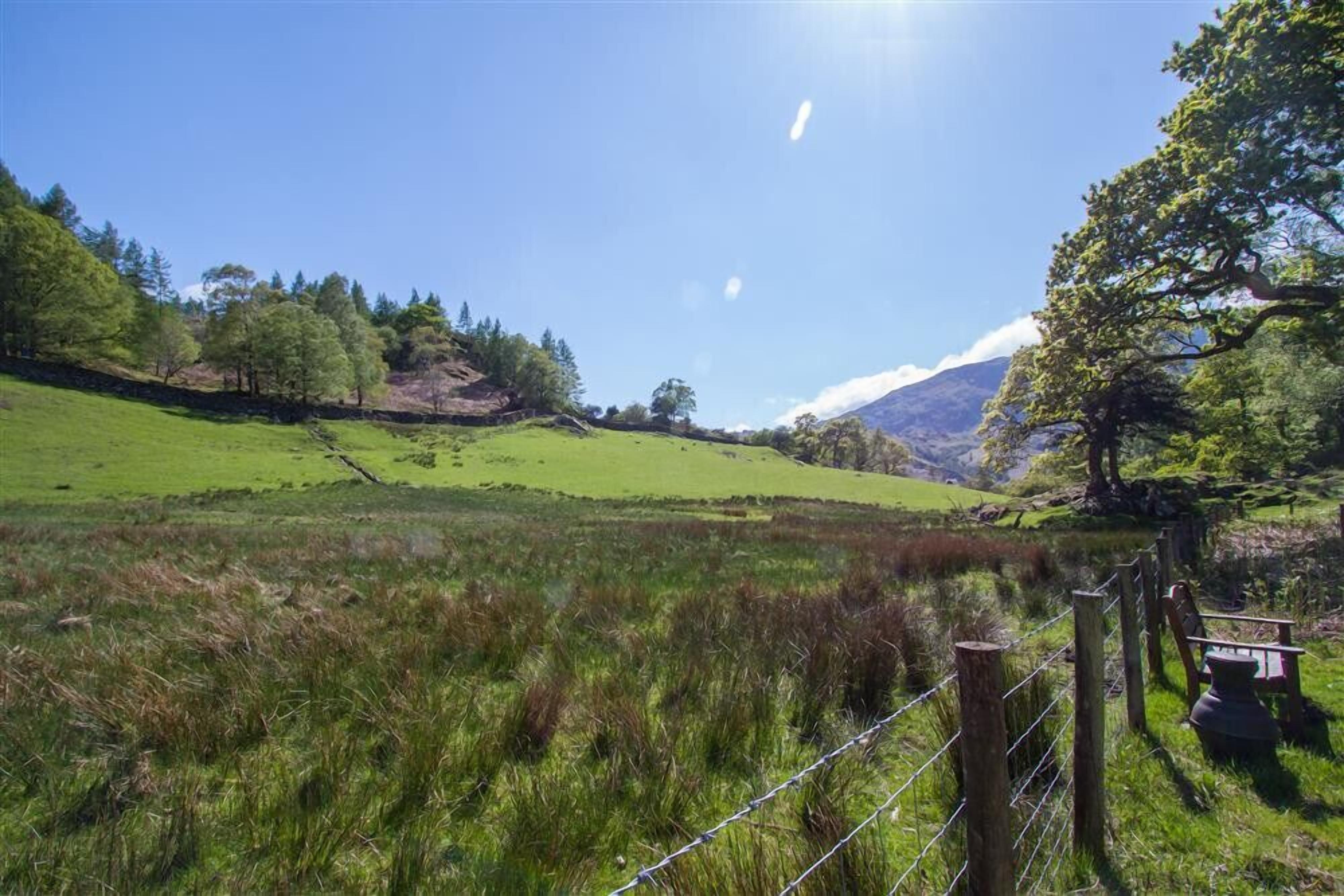 A rural landscape with a grassy field, a wooden fence, and a bench.