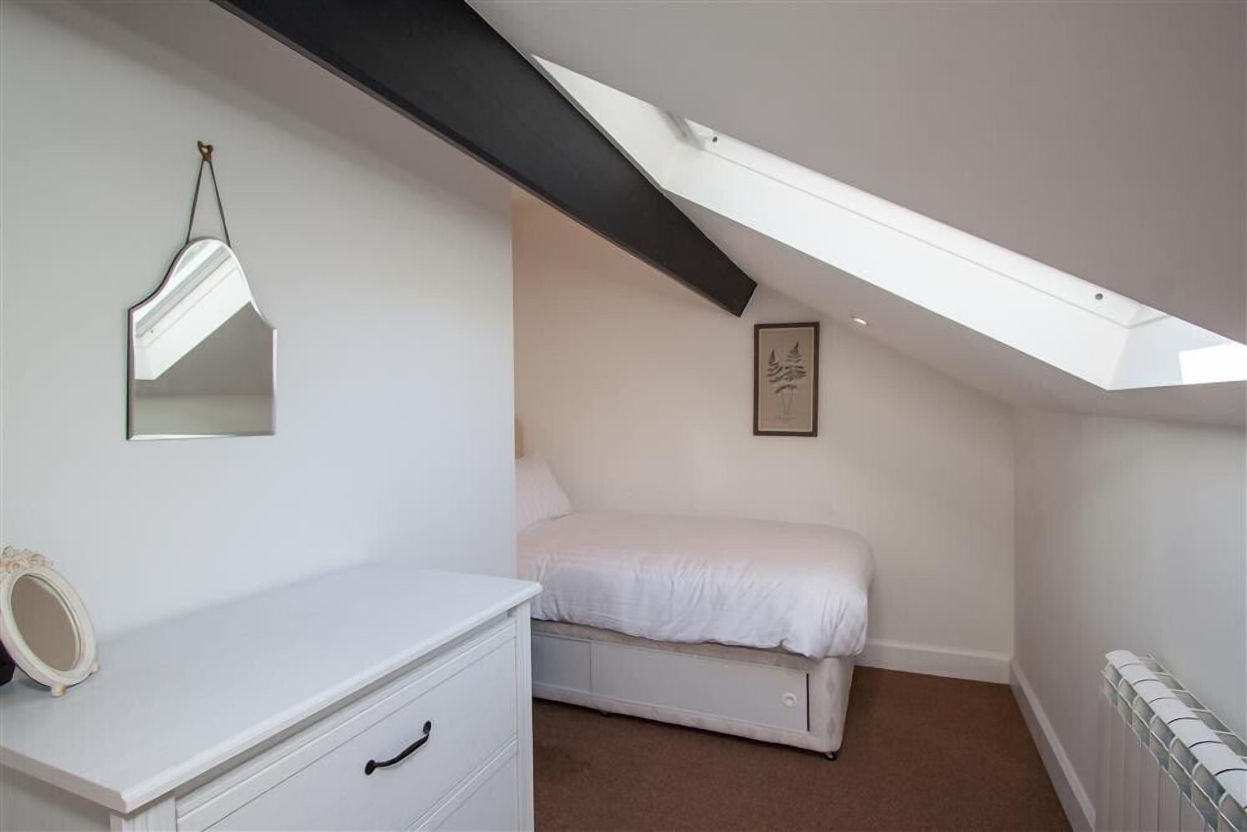 A bedroom with a sloped ceiling, a bed, a dresser, a mirror, and a framed picture on the wall.