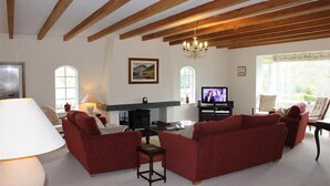Una sala de estar con sofás rojos, una chimenea, un televisor y vigas de madera en el techo.