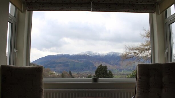 Una habitación con dos sillas y una mesita cerca de una ventana con vistas a una cadena montañosa.