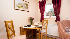Une pièce chaleureuse avec un bureau en bois, une chaise, un fauteuil à rayures, un vase de fleurs, un appareil photo et un tableau encadré accroché au mur.