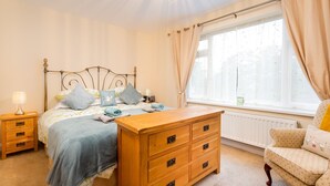 Une chambre à coucher avec un lit, une commode en bois, une table de chevet et une fenêtre avec des rideaux.