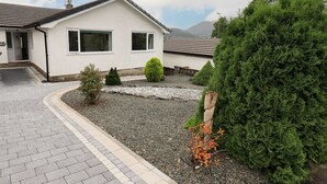 Ein Wohnhaus mit gepflasterter Auffahrt, Kiesgarten und einem großen immergrünen Baum.