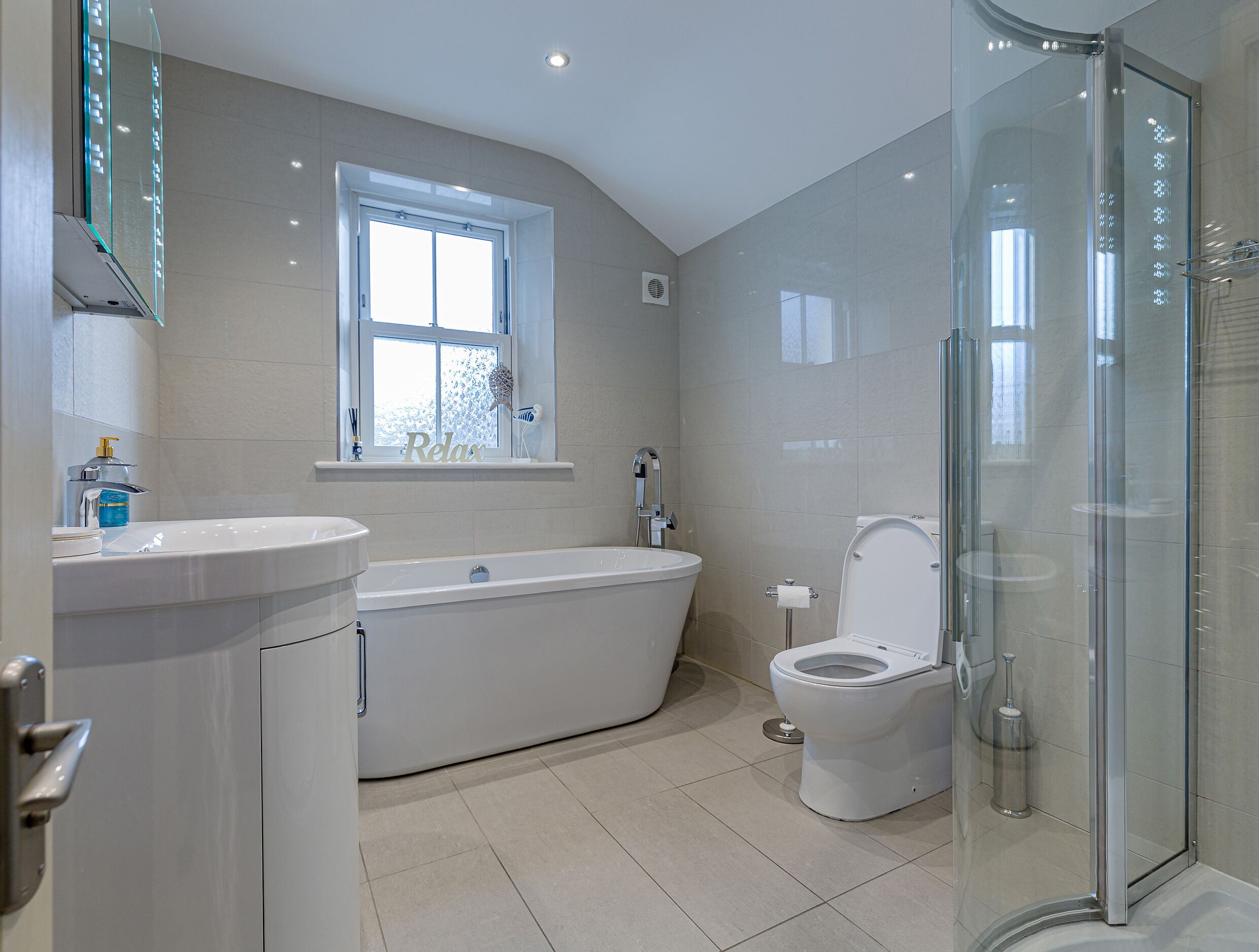 A modern bathroom with a bathtub, toilet, and glass shower enclosure.