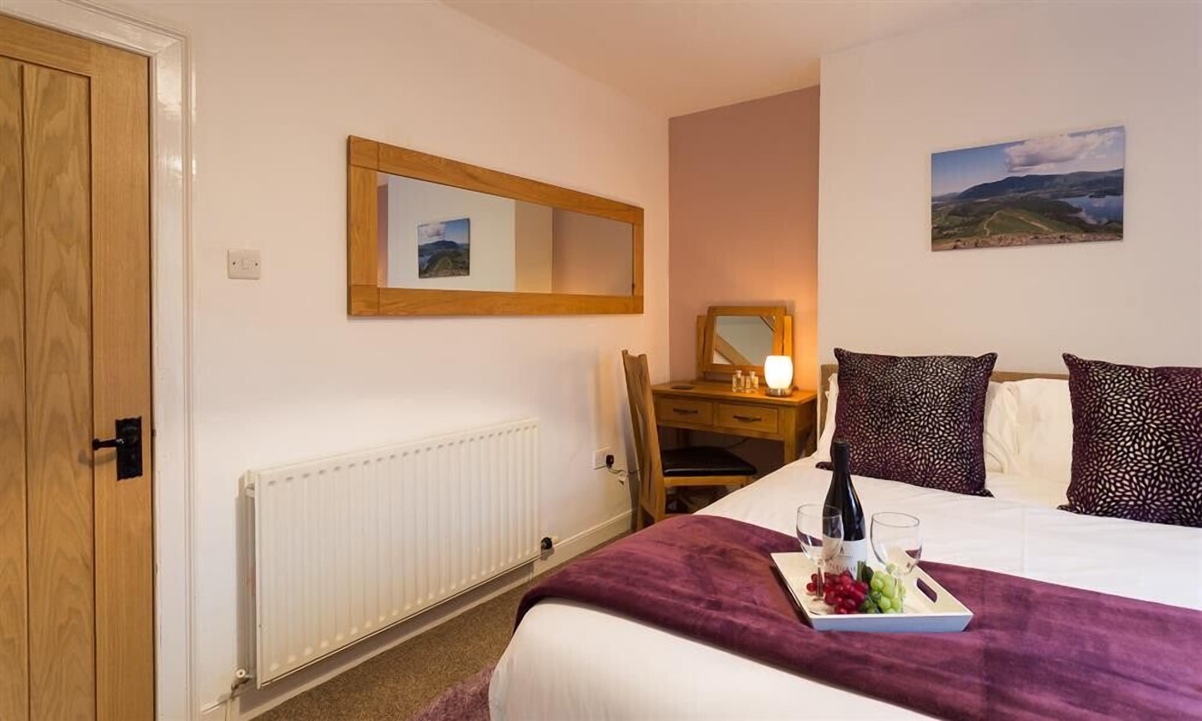 Une chambre d’hôtel avec un lit, un bureau et une chaise, un miroir, un radiateur et un tableau au mur.