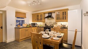 A modern kitchen with wooden cabinets, a gas stove, and a dining table set for four. - The Cats Bield (Keswick)