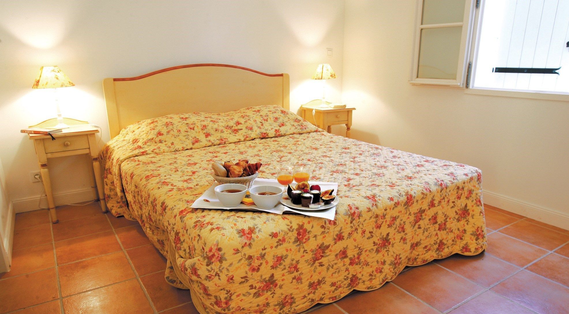 Una cama bien hecha con ropa de cama floral, dos mesitas de noche con lámparas y una bandeja de desayuno sobre la cama.