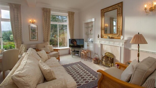 A spacious living room with a sofa set, a television, a fireplace, and a large mirror. - Betamere (Ambleside)