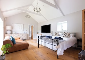 A spacious bedroom with a large bed, a wooden floor, a ceiling with skylights, and a modern chandelier.