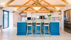 A modern kitchen with a central island, bar stools, and a large refrigerator. - The Farmhouse - Within the Helland Barton Farm Collection (Delabole)
