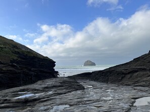 Paisagem costeira rochosa com uma formação rochosa proeminente ao longe, céu claro e vista do mar.
