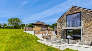 A modern house with a stone exterior, a large glass balcony, and a well-maintained lawn. - The Farmhouse - Within the Helland Barton Farm Collection (Delabole)