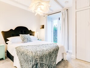Quarto com cama grande, mesa de cabeceira, luminária, janela com cortinas e porta.