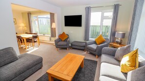 A modern living room with grey sofas, a wooden coffee table, and a dining area with a table and chairs. - Bowderstone (Keswick)