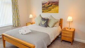 A neatly made bed with a rolled towel, two bedside lamps, and a landscape painting above the headboard. - Bowderstone (Keswick)