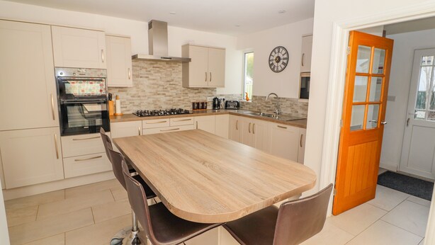 A modern kitchen with a central island, white cabinetry, and a wooden door. - Bowderstone (Keswick)