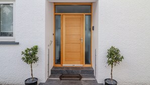 A wooden front door with a glass panel, a metal handle, and a keyhole. There are two potted plants on either side of the door. - Bowderstone (Keswick)
