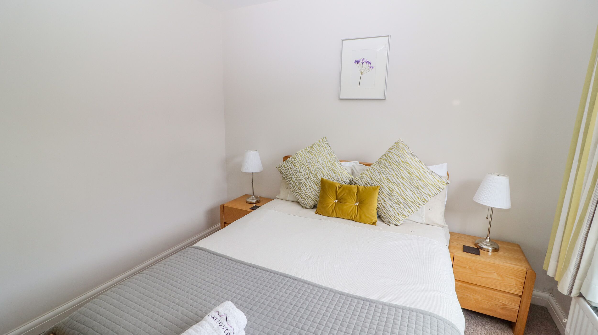Une chambre d’hôtel bien rangée, avec un lit, deux tables de chevet et un tableau encadré au mur.