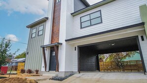 Une maison moderne à deux étages, dotée d’un garage, d’un élément décoratif vertical en bois bien visible sur le côté gauche et d’un toit plat.