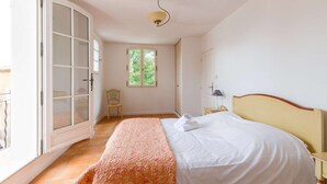 Un dormitorio con cama, ventana, silla y puerta que da a un espacio exterior.