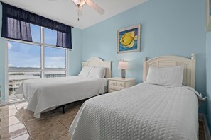 A hotel room with two beds, a ceiling fan, a window with a view, and a painting of a fish. - Crystal Shores West 101- Enjoy the View of Paradise (Gulf Shores)