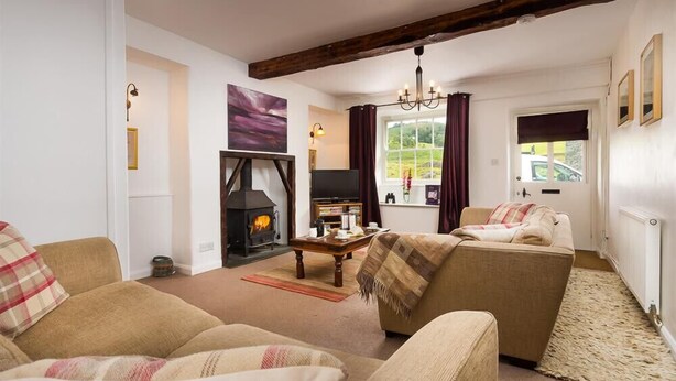 A cozy living room with a fireplace, a sofa, a television, and a window with curtains. - Pollys Cottage (Ambleside)