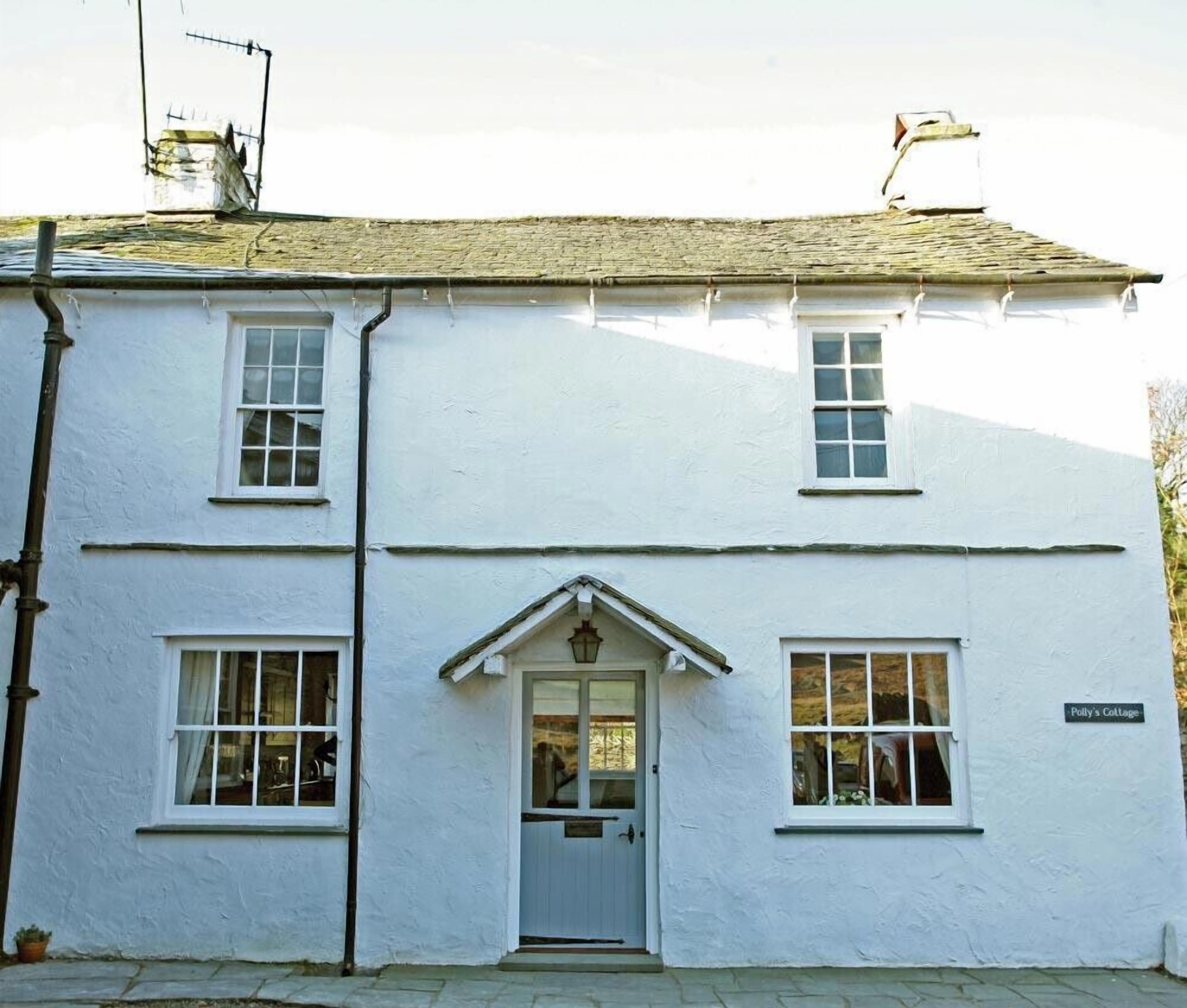 A white two-story building with a central entrance, a small porch, and a sign reading "Polly's Cottage".