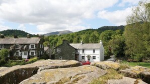 A stone building with a white facade, surrounded by large rocks and greenery. - Pollys Cottage (Ambleside)