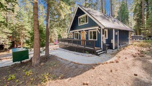 A cabin with a porch, surrounded by tall trees. - Cobalt by Tahoe Getaways - Luxury 3BR w/ Hot Tub, Walk to Lake - Dog OK (Carnelian Bay)