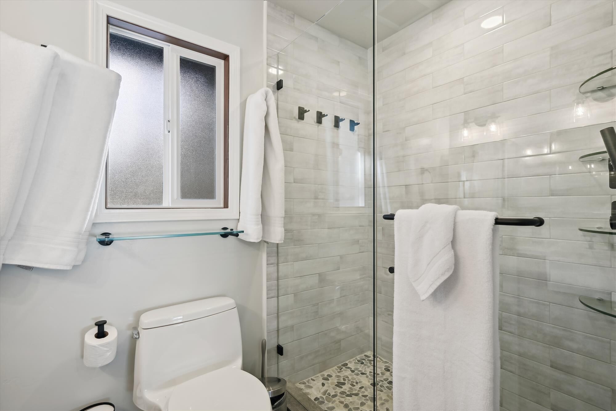 A modern bathroom with a glass shower enclosure, a toilet, and a glass sink.