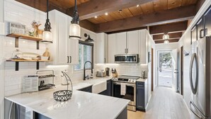 A modern kitchen with white cabinets, a central island, stainless steel appliances, and wooden ceiling beams. - Cobalt by Tahoe Getaways - Luxury 3BR w/ Hot Tub, Walk to Lake - Dog OK (Carnelian Bay)