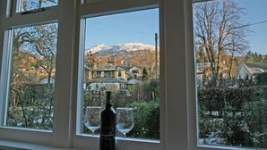 Ein Zimmer mit großen Fenstern und Blick auf einen schneebedeckten Berg sowie ein Dorf darunter.