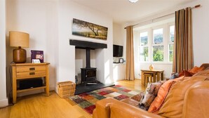 Ein gemütliches Wohnzimmer mit Kamin, Fernseher, einer Couch und einem Fenster mit Vorhängen.