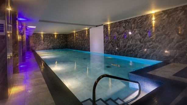 A modern indoor swimming pool with a clear blue water surface, surrounded by stone walls and equipped with a pool ladder. - Brooklands (Ambleside)