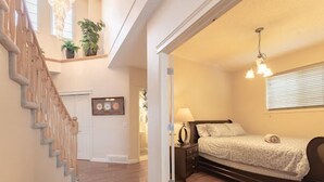 Ein Schlafzimmer mit Bett, Nachttisch, Lampe und Blick auf den Flur.